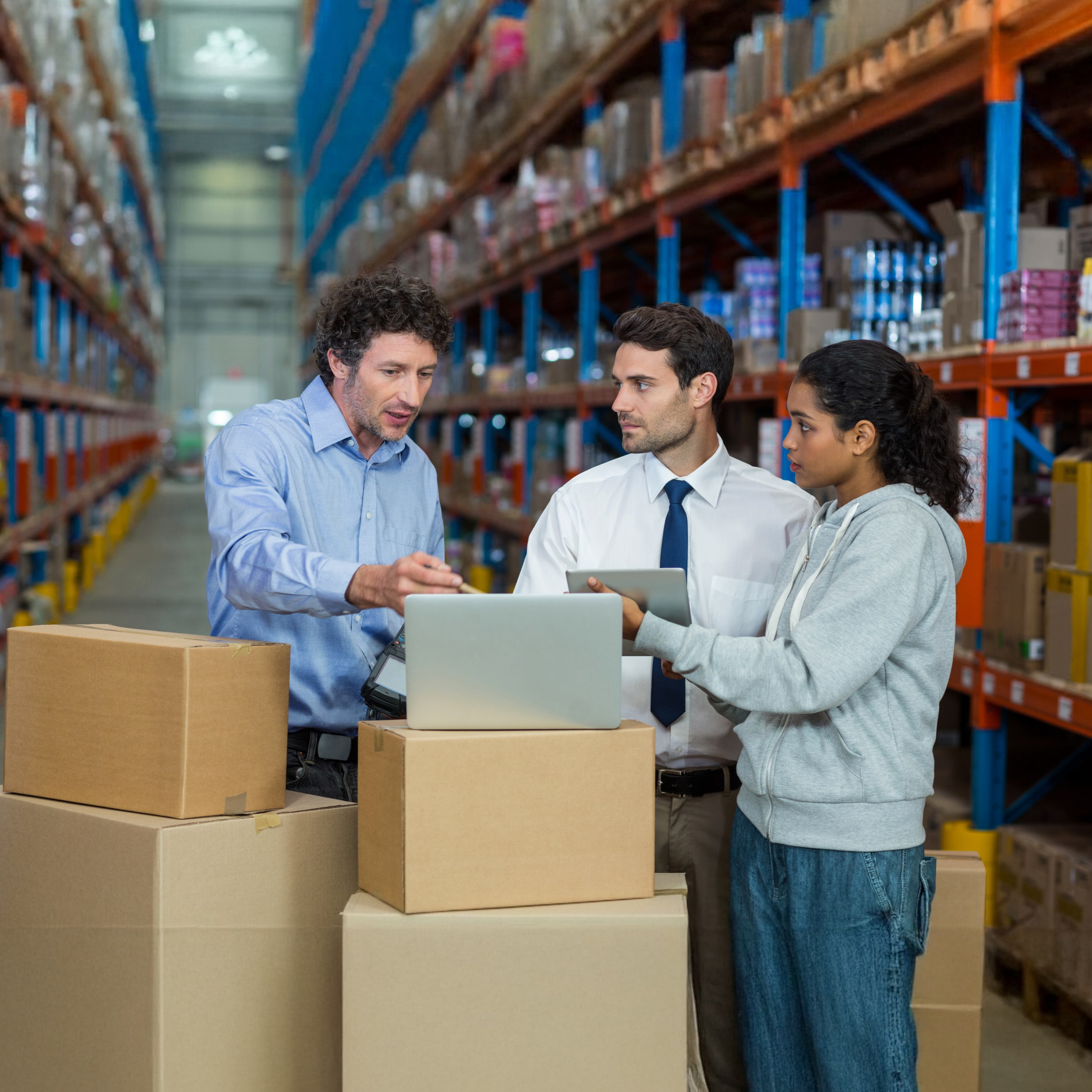 Logistics professionals coordinating customs clearance and freight forwarding processes in a warehouse environment, surrounded by boxes and storage shelves.